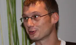 Sladjan Osmanagic, en man med glasögon, ler mot kameran. Bakom honom syns gröna växter.