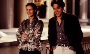 Julia Roberts young och Hugh Grant skrattar tillsammans utomhus.