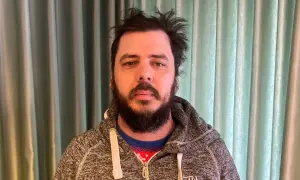 Man med rufsigt hår och skägg, klädd i en grå hoodie över en julig tröja. Han ser ut att ha haft en chang frick.