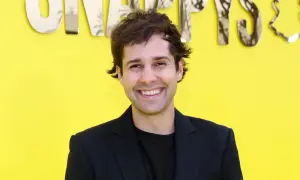David Dobrik ler framför en gul bakgrund med texten "Snapchat". Kanske han vet hur man får alla trofeer på Snap?
