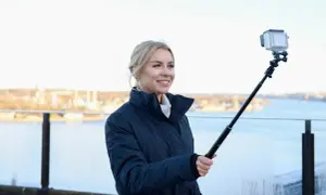 Therese Lindgren filmar med GoPro på selfiepinne vid en vattensamling med stad i bakgrunden.