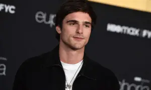 Jacob Elordi style: en ung man med mörkt hår och en vit t-shirt under en svart jacka, med en silverhalsband.