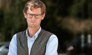 Claes de Faire, en man med glasögon och en väst, ler mot kameran utomhus.
