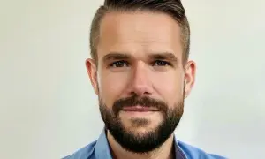 Johnny Kroneld, en man med kortklippt mörkt hår och skägg, bär en blå skjorta.