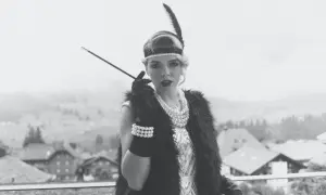 Kvinna i 1920-talsmode med fjäderpannband, pärlhalsband och cigaretthållare.