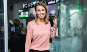 Jennie Pierrou ler vid en glasdörr i en kontrollrumsmiljö med många skärmar.
