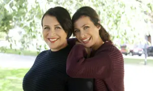 Två leende kvinnor, Hannah och Amanda, står nära varandra utomhus.