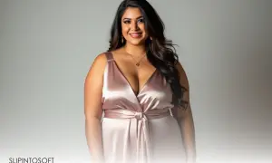 En leende plus size modell i en glänsande rosa klänning med djup urringning och knyt i midjan.