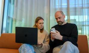 Man och kvinna sitter i soffa med laptop och mobil. De verkar diskutera något från samtiden tidning.