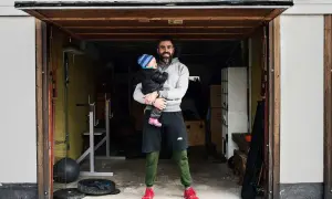 Man holding a baby in a garage with gym equipment.