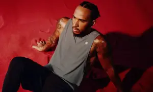Lewis Hamilton visar upp sin Lewis Hamilton fashion-stil i en grå linne och svarta byxor, sittandes på en röd yta.