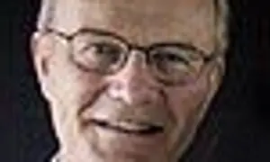 Närbild på Olle Stenholm med glasögon, ett vänligt leende och mörkt bakgrund.