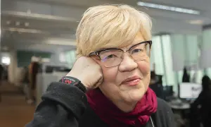 Lena Mellin med glasögon och en vinröd scarf vilar huvudet i handen.