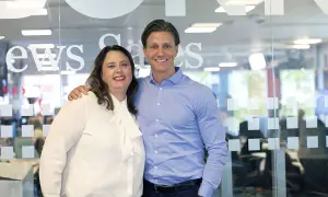 Anna Hjalmarsson och en kollega ler mot kameran framför en glasvägg med texten "News Games".