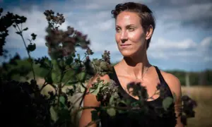 Elin Kjos, med kortklippt hår, blickar ut över ett fält. Blommor i förgrunden skapar en naturlig inramning.