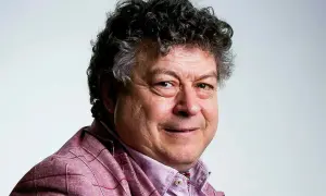 Rory Sutherland, med sitt karaktäristiska lockiga hår och ett vänligt leende, bär en rutig kavaj.