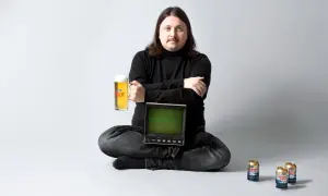 Man med mustasch sitter med en öl i handen och en gammal datorskärm. Norrlands Guld reklam.