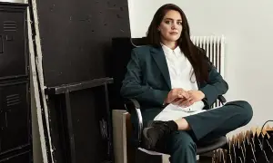 Jenny Nordlander sitter i en stol, klädd i kostym. Bakom henne syns svarta skåp och en vit vägg med element.
