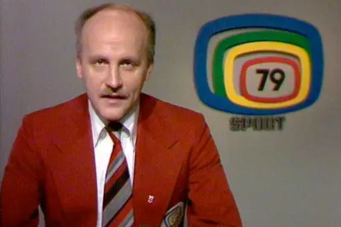 Arne Hegerfors i röd kavaj med slips, bredvid en logotyp med siffran 79 och texten SPORT.