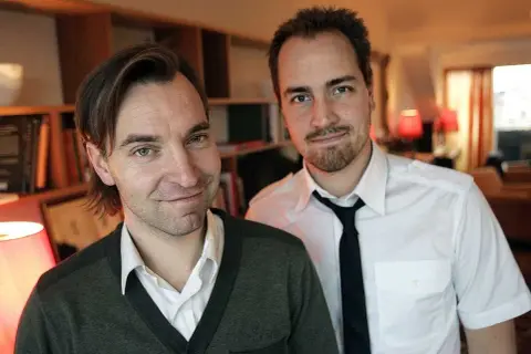 Två män, varav en är Måns Mårlind, poserar framför bokhyllor.