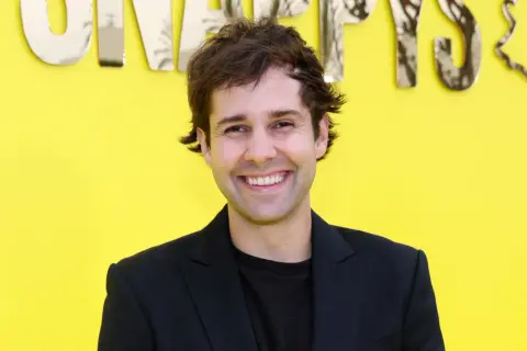 David Dobrik ler framför en gul bakgrund med texten "Snapchat". Kanske han vet hur man får alla trofeer på Snap?