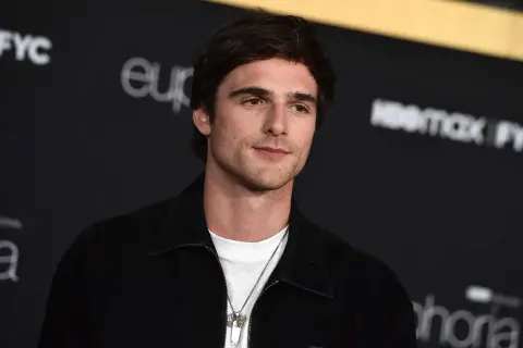 Jacob Elordi style: en ung man med mörkt hår och en vit t-shirt under en svart jacka, med en silverhalsband.