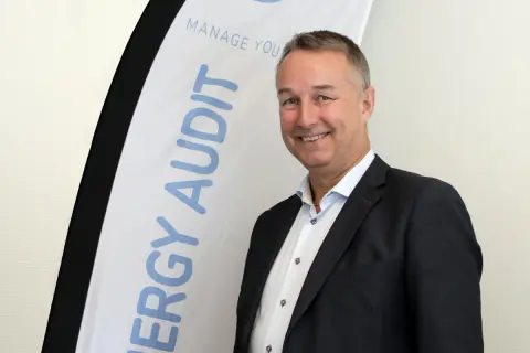 Thomas Ekman ler glatt framför en banderoll med texten "ENERGY AUDIT".