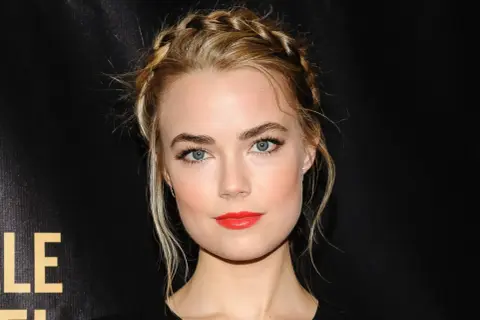 Rebecca Rittenhouse med flätat hår och rött läppstift, blickar mot kameran.