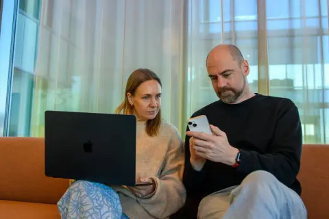 Man och kvinna sitter i soffa med laptop och mobil. De verkar diskutera något från samtiden tidning.
