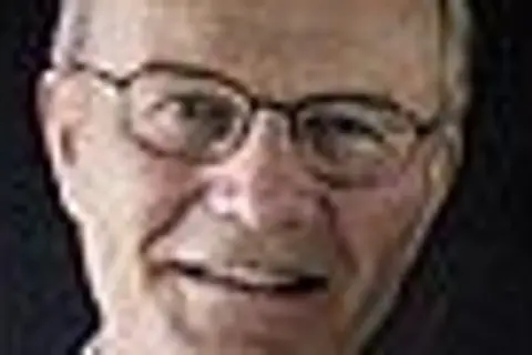 Närbild på Olle Stenholm med glasögon, ett vänligt leende och mörkt bakgrund.