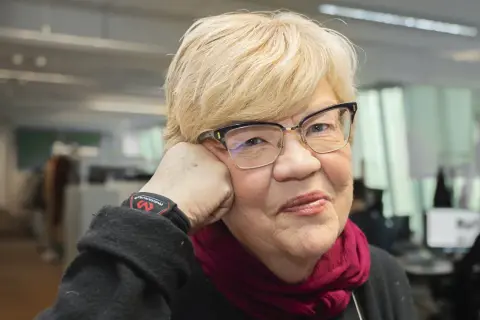 Lena Mellin med glasögon och en vinröd scarf vilar huvudet i handen.