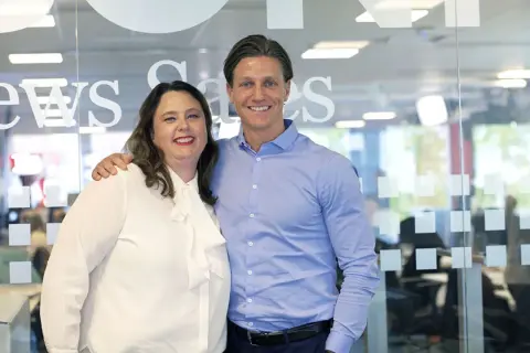 Anna Hjalmarsson och en kollega ler mot kameran framför en glasvägg med texten "News Games".