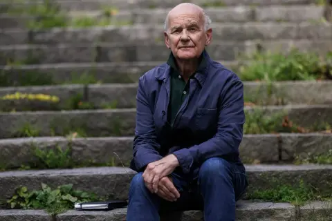 Johan af Donner sitter på en trappa utomhus, klädd i en mörkblå jacka och jeans. En anteckningsbok ligger bredvid honom.