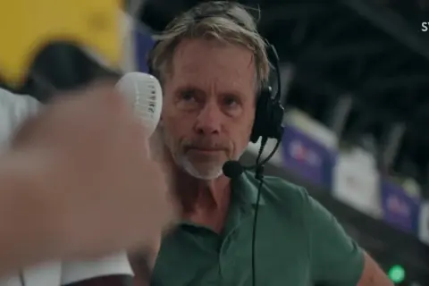 En svt sport medarbetare med headset och mikrofon, redo att rapportera från en sportarena.