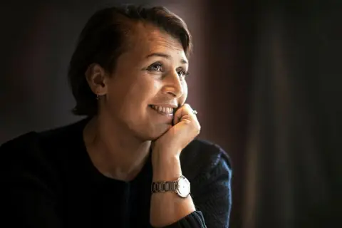 Hanna Widell ler och vilar hakan i handen, klädd i en mörk tröja med en klocka på handleden.