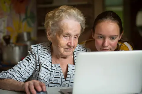 En äldre kvinna och en ung flicka tittar på en laptop. De lär sig om nya medier, en kontrast till traditionella medier.