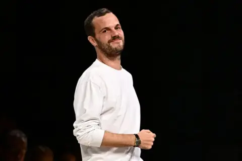 Matthieu Blazy, klädd i en vit långärmad tröja, ler mot kameran.
