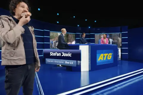 Man äter korv i en studio med ATG-reklam.