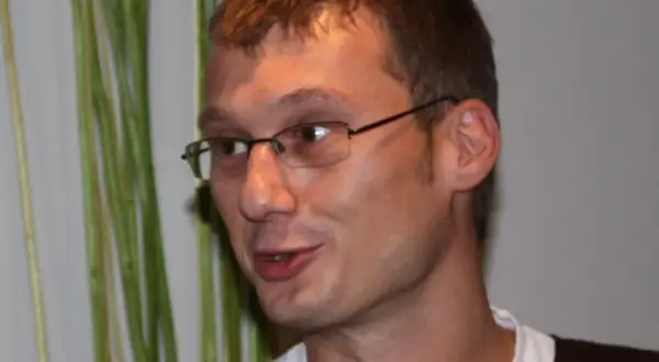 Sladjan Osmanagic, en man med glasögon, ler mot kameran. Bakom honom syns gröna växter.