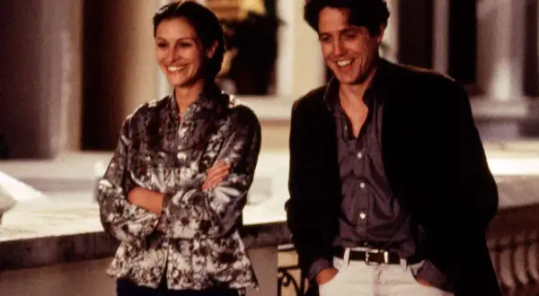 Julia Roberts young och Hugh Grant skrattar tillsammans utomhus.