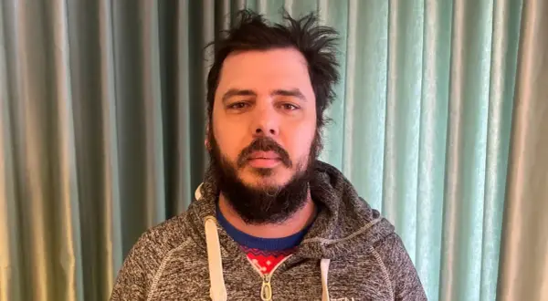 Man med rufsigt hår och skägg, klädd i en grå hoodie över en julig tröja. Han ser ut att ha haft en chang frick.
