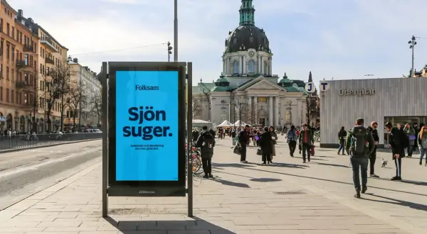 Folksam reklam på en blå skylt i en stadsmiljö. "Sjön suger" står det, med texten "Sparande och försäkring ska inte göra det." under.