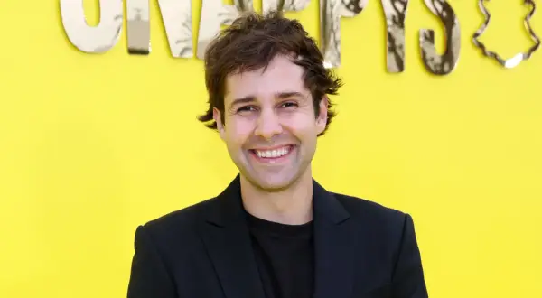 David Dobrik ler framför en gul bakgrund med texten "Snapchat". Kanske han vet hur man får alla trofeer på Snap?