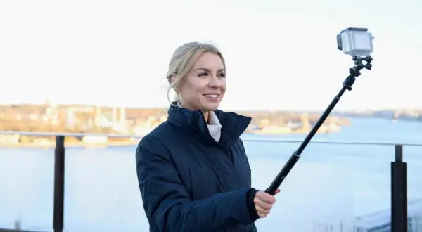 Therese Lindgren filmar med GoPro på selfiepinne vid en vattensamling med stad i bakgrunden.