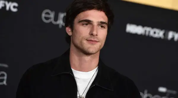 Jacob Elordi style: en ung man med mörkt hår och en vit t-shirt under en svart jacka, med en silverhalsband.
