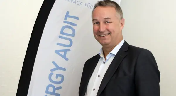 Thomas Ekman ler glatt framför en banderoll med texten "ENERGY AUDIT".