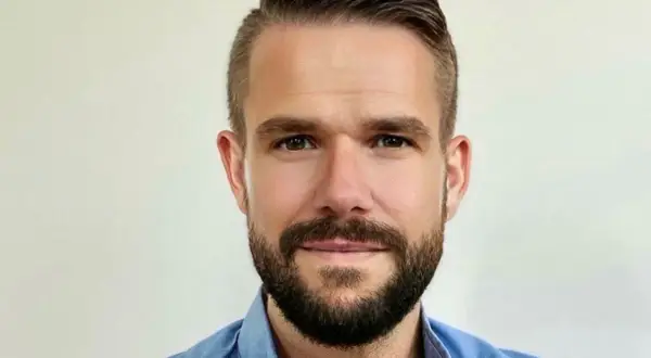 Johnny Kroneld, en man med kortklippt mörkt hår och skägg, bär en blå skjorta.