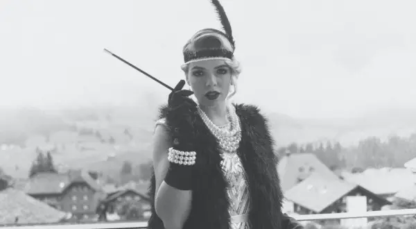 Kvinna i 1920-talsmode med fjäderpannband, pärlhalsband och cigaretthållare.