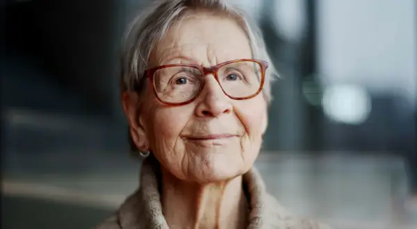 Kerstin Brunnberg, en äldre kvinna med glasögon och grått hår, ler mjukt.