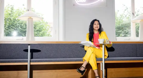 En pr specialist i gul dräkt sitter med papper och kaffe.